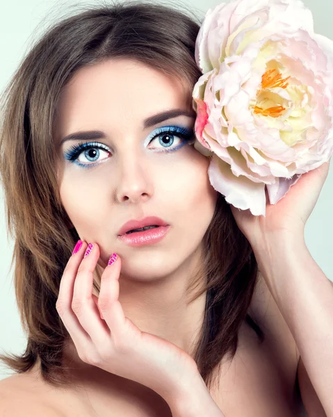 Schöne junge Frau mit blauen Augen, langen Wimpern und rosa Nägeln. Blume im Haar. — Stockfoto