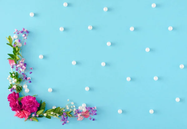 Creative and unique spring concept made with flowers, leaves and white pearls on pastel blue background. Beautiful and elegant idea for wallpaper. Minimal flat lay.