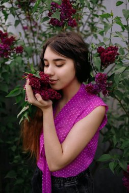 Parktaki leylak çalılarının yanında duran kızıl saçlı genç kız.