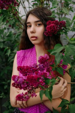 Parktaki leylak çalılarının yanında duran kızıl saçlı genç kız.