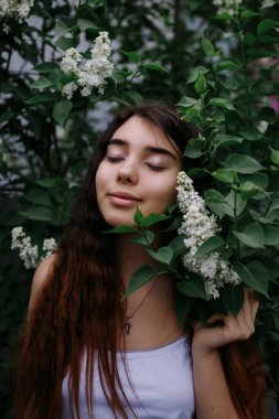 Parktaki leylak çalılarının yanında duran kızıl saçlı genç kız.