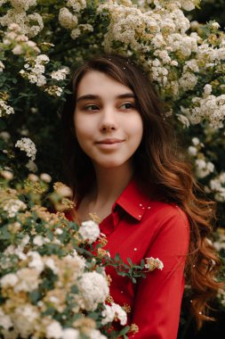 Güzel kızıl saçlı genç kız baharda kırmızı bir bluz içinde, çiçek açan çalıların yanında.