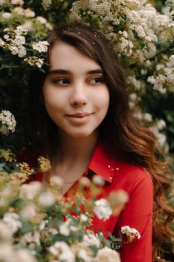 Güzel kızıl saçlı genç kız baharda kırmızı bir bluz içinde, çiçek açan çalıların yanında.