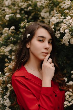 Güzel kızıl saçlı genç kız baharda kırmızı bir bluz içinde, çiçek açan çalıların yanında.