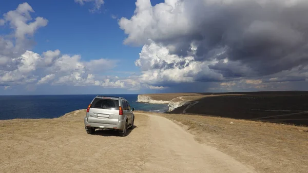 Off-road car and a cliff over the Black Sea under the oncoming storm clouds, Tarkhankut coast, Crimean Peninsula in Russia.
