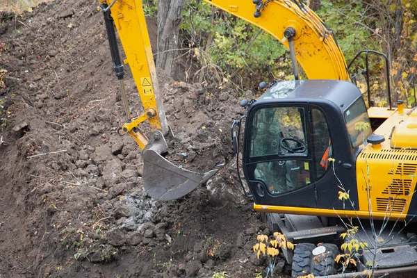 The excavator works on a construction site, lifting a bucket full of soil.