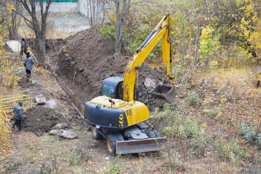 Bir inşaat sahasında bir kazıcı ve işçiler inşaat bariyerleriyle çit kazıyorlar, kentsel su şebekesinde onarım çalışmaları, şehirdeki ısıtma ağlarının onarımları.