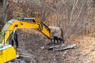The bucket of a backhoe excavator is raised above a concrete slab on a construction site in autumn, excavator operation for cleanup in construction, various tasks for excavators.