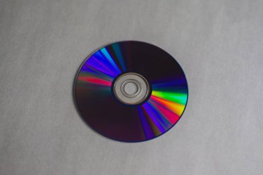 Gri arka planda gökkuşağı çizgileri olan kompakt bir diskin yakın çekimi. Işık yansımaları dinamizm duygusu yaratır ve hala estetikleriyle büyüleyen geçmişin teknolojilerini sembolize eder..