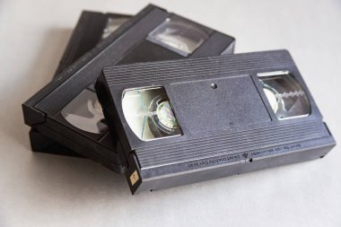 Üç eski VHS kaseti yakın planda gri bir masanın üstünde duruyor. Dijital çağ ve video kasetlerinin günlük hayatın önemli bir parçası olduğu zamanlar..