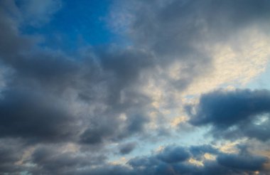 Bulutların rüzgarın etkisi altında şekil değiştirdiği gri ve mavi bulutların gölgeleriyle gökyüzü. Esnekliği ve adaptasyonu sembolize eder.
