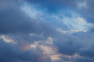 Güneş ışığı mavi-gri bulutları delip geçer, gökyüzünü altın parıltılarla aydınlatır. Karanlık zamanlarda umudu ve ışığı simgeler..
