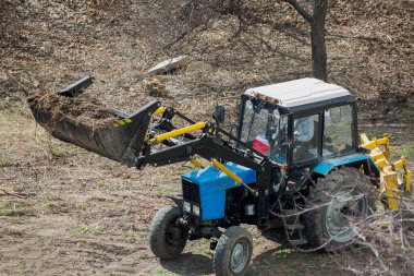 Yüksek bir kova taşıyan, enkaz ve odun atığı taşıyan inşaat yükleyicisi bölgeyi temizliyor. Peyzaj çalışmaları devam ediyor.