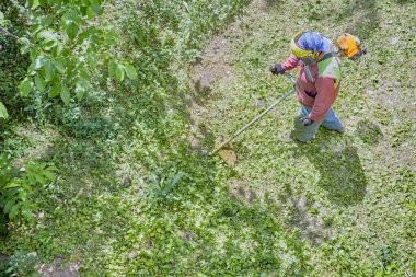 Kasklı ve tulumlu profesyonel bir bahçıvan çim biçme makinesiyle çimleri biçiyor..