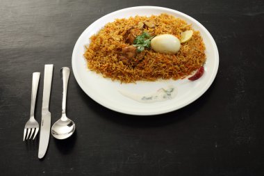 Beyaz tabakta yumurta ve siyah arka planda tavuk biryani.