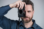 Fotograf středního věku fotografovat s pohledem na šedé pozadí fotoaparátu, snímek.