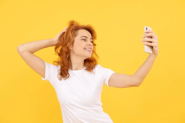 一个兴奋而快乐的年轻女子被隔离在黄色的背景下的形象用相机拍成了自拍 红头发的女孩 — 图库照片