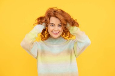 Güzel, kızıl saçlı, kıvırcık saçlı, gülümseyen, sarı arka planda kameraya bakan güzel bir kızın portresi.