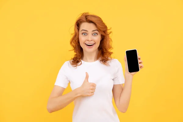 兴奋的年轻女子用手机在黄褐色的背景上表现出不错的手势 红头发的女孩 — 图库照片