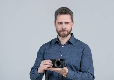 Sıradan tişörtlü sakallı adam. Elinde aralık bulucu fotoğraf makinesi, elinde gri arka plan, fotoğrafçılık..