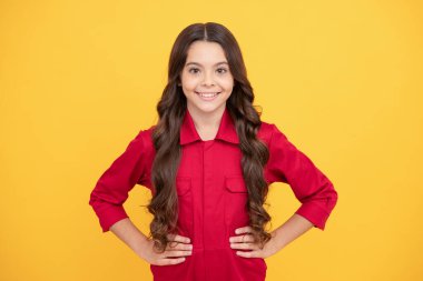 Kendine güvenmek. Mutlu çocukluk. Uzun kıvırcık saçlı neşeli genç kız. Çocuk sarı arka planda kırmızı gömlek giyiyor. Çocuk mutluluğu ifade eder. pozitif duygular. Güzel gülümseyen çocuk.