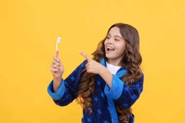 Buraya bak. Pijamalı çocuk sabah rutinini yapıyor. Diş bakımı. Sağlıklı güzel gülümseme. En iyi diş macununu kullanarak. Çocukların stomatolojisi. Genç kız parmak diş fırçasını işaret ediyor. Mutlu çocuk dişlerini fırçalayacak..