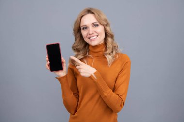 Özelliklerle dolu. Mutlu kız cep telefonunu işaret ediyor. Reklamcılık için işaret parmağı. Modern teknoloji. Kopyalama alanı için boş akıllı telefon ekranı.