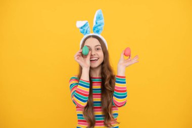 Mutlu Paskalyalar. çocukluk mutluluğu. Tavşan kulaklı çocuk boyalı yumurtaları tutuyor. Eğlence zamanı. Yumurta avındaki sevimli komik çocuk. Paskalya bahar tatili. Mutlu genç kız tavşan kulağı takar.