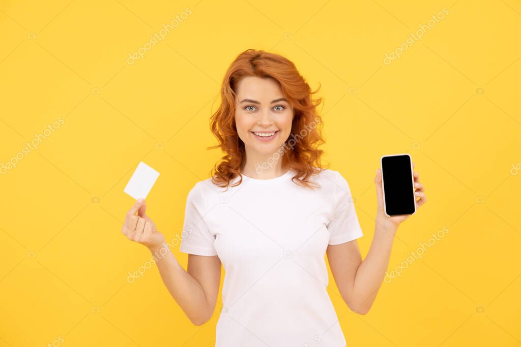 happy redhead woman showing credit or debit card and smartphone to make online shopping, online banking.