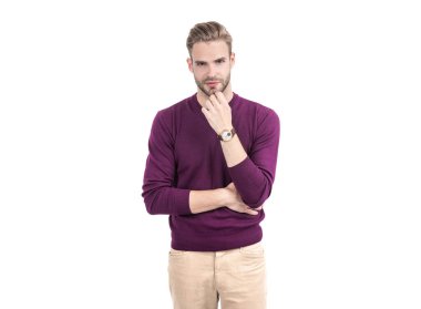 Tıraşsız yüzü olan yakışıklı bir adam mor kazak giyer, beyaz ve trende izole edilmiş sıradan pantolonlar giyer..