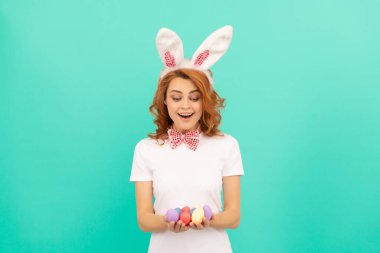 Paskalya eğlencesi. Eğlence zamanı. Yumurta avı. Sevimli bayan komik görünüyor. Paskalya bahar tatili. Kızıl saçlı kadın boyalı yumurtaları tutuyor. Mutlu kız tavşan kulağı takar. Mutlu Paskalyalar. Tavşan kulaklı ve papyonlu kadın..