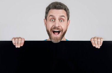 Reklam için fotokopi alanı olan şaşırmış bir adam. Reklamcılık. Duyuru. Alışveriş ve indirim. ürün sunumu. Yenilik bilgisi sunuyorum. Siyah kağıdın arkasında hayrete düşmüş bir erkek..