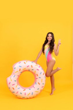 Havuz partisi için havuz yüzüğüyle mayo giymiş mutlu bir sahil çocuğu. Yaz tatilinde sarı arka planda, mayo..