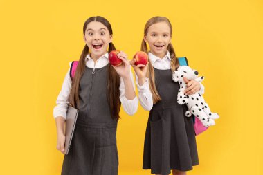 Resmi üniformalı okul çocukları ağızlarını açık tutarlar. Doğal elmalar, sarı arka plan, sağlıklı beslenme..