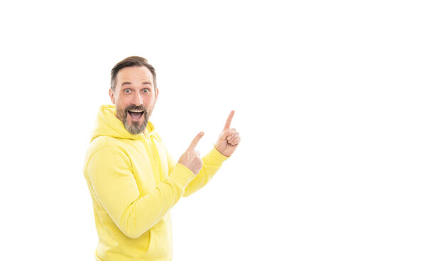 Реклама вашего бренда. реклама для взрослых. скопировать пространство. Взрослый удивленный мужчина указывает пальцем. Улыбающийся старший парень представляет продукт, изолированный на белом. советник в желтой толстовке.