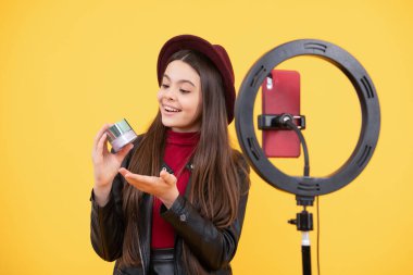 Mutlu genç kız blogcu, makyaj malzemesi ve moda sunan çevrimiçi video dersi güzellik blogu hazırlamak için tripoda selfie kabartmalı lamba ve akıllı telefon kullanıyor..