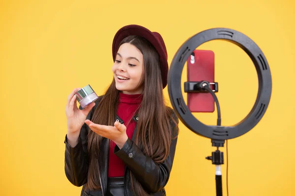 Mutlu genç kız blogcu, makyaj malzemesi ve moda sunan çevrimiçi video dersi güzellik blogu hazırlamak için tripoda selfie kabartmalı lamba ve akıllı telefon kullanıyor..