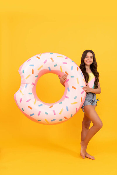 happy beach teen girl with curly hair with donut inflatable ring for pool party fun on summer vacation on yellow background, summertime.