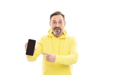 Reklam sunumu. kopyalama alanı. Olgun, mutlu adam telefon ekranını sunuyor. Beyazda izole akıllı telefon gösteren gülümseyen son sınıf öğrencisi. Sarı kapüşonlu ponpon parmaklı adam. ürün önerisi.