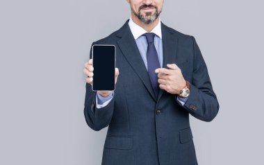 Ürün teklifi. Reklam sunumu. kopyalama alanı. Adam telefon ekranını sunuyor. Kesilmiş adam gri arka planda akıllı telefon gösteriyor. İş adamı kılığındaki adam cep telefonu cihazını işaret ediyor..
