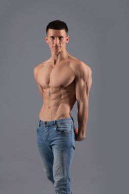 Kas zindeliği. Formda adam üstsüz gri arka plan pozu veriyor. Gövdesi kaslı vücut geliştirici. Altılı karın kası eğitimi. Fiziksel fitness ve spor. Vücut geliştirme. Kas yapısı geliştiriliyor.