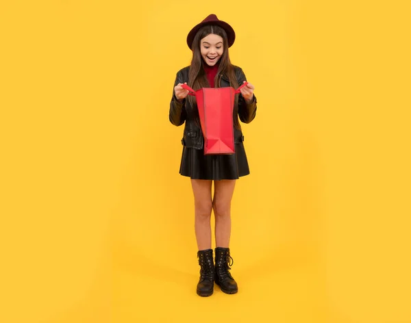 fall seasonal sales. back to school. tween fashion look. childhood. surprised girl in leather carry present. stylish teen child shopping. kid in hat look inside shopping bag. autumn season trends.