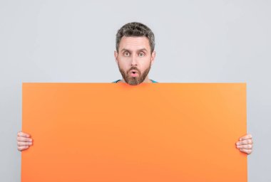 Reklam için fotokopi alanı olan şaşırmış bir adam. Reklamcılık. Duyuru. Alışveriş ve indirim. ürün sunumu. Yenilik bilgisi sunuyorum. Turuncu kağıdın arkasındaki hayret verici erkek..