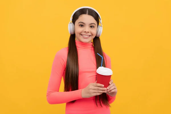 Gelukkig kind luisteren muziek in hoofdtelefoon met papieren beker op gele achtergrond, levensstijl — Stockfoto