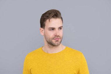Yakışıklı bir genç adam portresi, traşsız, sarı süveter, gri arka plan, yakışıklı.