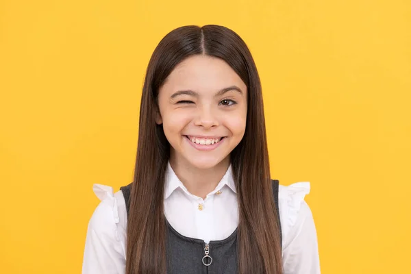 Feliz niña en edad escolar con la cara sonriente dar guiño fondo amarillo, guiño — Foto de Stock