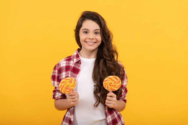 Gelukkig kind met lang krullend haar in shirt houden lolly karamel snoep op gele achtergrond, lekker. — Stockfoto