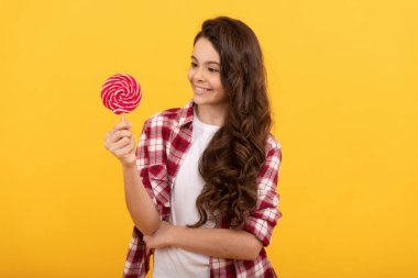Uzun kıvırcık saçlı neşeli çocuk sarı arka planda lolipop karamel şekeri, diş sağlığı.