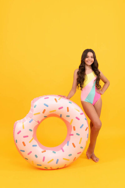 beach teen girl in swimsuit with doughnut inflatable ring on yellow background, beach accessory.