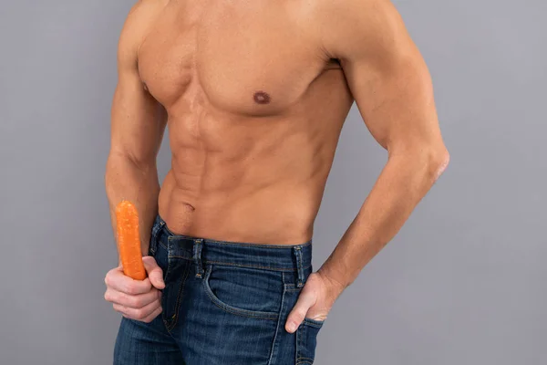 Healthy man with fit torso hold carrot as penis. Sexual potency. Sexual arousal. Erection.